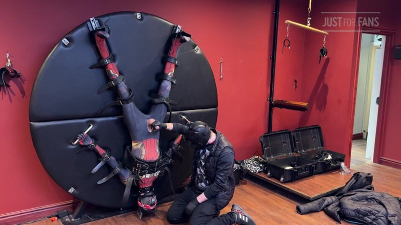 Inmate Cody and SubEdgeX: Pup Twink, одягнений як людина-павук, прив'язаний до бондажного колеса і доїв
